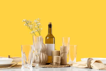 Fotobehang Eetkamer Elegant festive table setting with wine bottle, glasses, candles and flowers on yellow background, modern dining decor for celebration, dinner party or holiday gathering  © Pixel-Shot