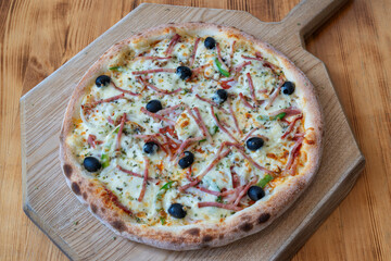 Delicious pizza topped with ham, olives, and green peppers on a wooden board, showcasing a mouthwatering culinary delight for food lovers