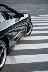 Close-up side view of a black sports car on a striped traffic island. Automotive detail vertical shot - sleek right hand drive car