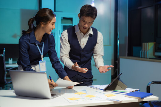 Financial analysts work overtime analyzing data on tablets, laptops, and graphs. Collaboration, teamwork, and planning.