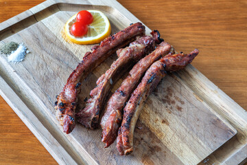 Juicy grilled ribs served on a wooden platter with lemon and cherry tomato, showcasing delicious barbecue flavors and vibrant presentation