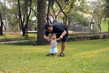 A father is teaching his child to walk on the grass