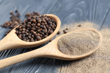 Spoons with black pepper powder and peppercorns on dark wooden background
