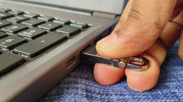 Close up of hand input pen drive, flash drive or thumb drive external storage and data transfer drive into laptop computer USB port hole. Small portable technology accessory or equipment concept.