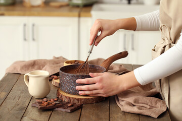 Woman stirring delicious chocolate sauce in bowl with whisk on table in kitchen. Closeup