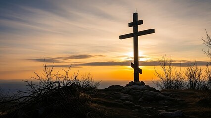 cross silhouette standing on a rocky hilltop illuminated by a vibrant, golden orange sunset or sunrise