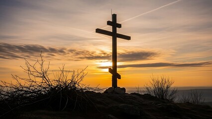 cross silhouette standing on a rocky hilltop illuminated by a vibrant, golden orange sunset or sunrise
