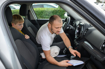 Obraz premium Father and son reading a car manual and setting hazard lights, learning vehicle safety together, family moment and responsible driving concept