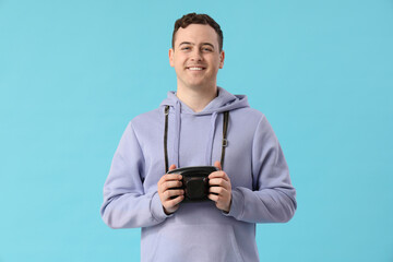 Young man with photo camera on blue background. Travel concept