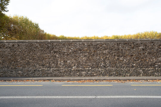 A solid stone wall adorned with fallen leaves, representing a strong boundary while embracing the vibrant hues of autumn in the environment surrounding it.