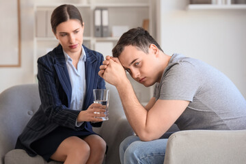 Male drug addict receiving glass of water from psychologist in office