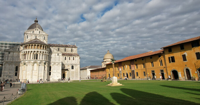 View of the Piazza dei Miracoli with its marble facade contrasting against the vibrant green lawn under a cloudy sky, Pisa, Tuscany, Italy.