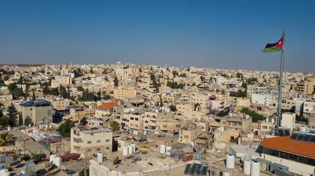 Morning panorama of Madaba, Jordan, with sunlight washing over rooftops and rolling hills, while the Jordanian flag waves softly above the cityscape