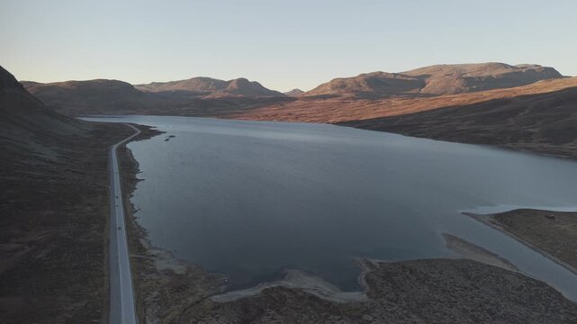 Panoramic view of mountain lake, surrounding mountains and a road along the lake. Drone footage, Norway
