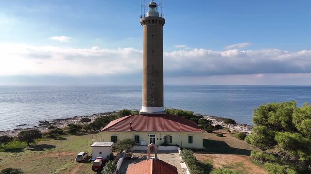 Drone lifts through pine trees to reveal a small chapel and the Veli Rat lighthouse on Dugi Otok, with the blue Adriatic Sea in the background.
