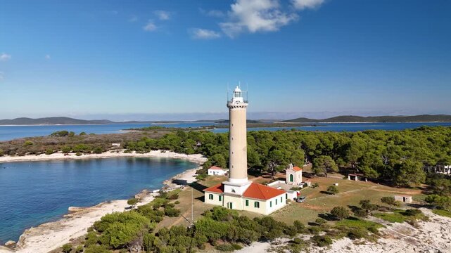 Aerial backwards reveal drone footage of the Veli Rat lighthouse on Dugi Otok, Croatia. Scenic rocky coastline, clear turquoise Adriatic Sea, and bright sunny weather in Zadar county.
