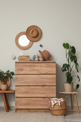 Interior of living room with hanging mirror, houseplants and home decor on commode near grey wall