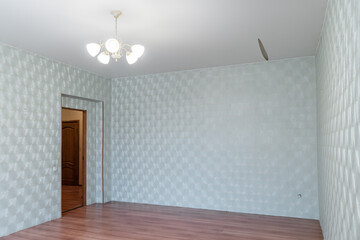 an empty room with an old renovation. There are old patterned wallpaper on the walls. The room has a wooden floor and a white ceiling. The light is pouring out of the window.