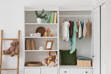 Closet with baby clothes, toys and books in nursery