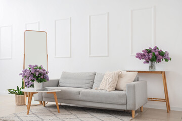 Interior of living room with sofa, mirror and lilac flowers in vases