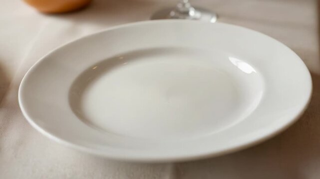 Shifting camera revealing white plate centered on table for service with wine glass and bread roll