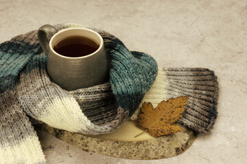 A maple leaf, tea, and a knitted scarf create an autumnal mood. A cozy mood for autumn. Autumn makes you want to warm up.