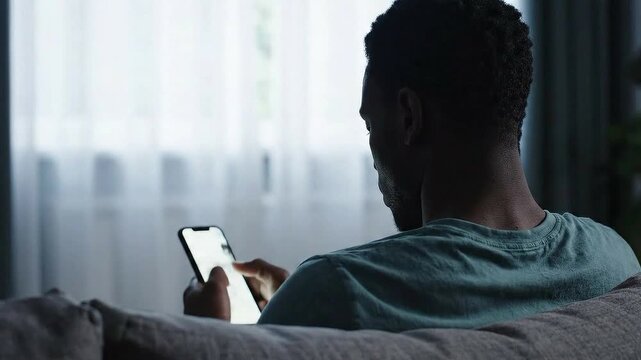 Man Relaxing on Sofa Using Smartphone Screen Glow Illuminates Face Soft Natural Light From Window