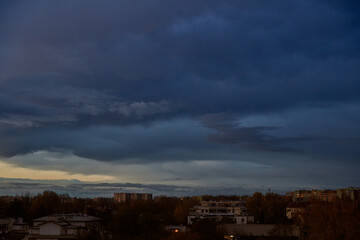 Dark, heavy storm clouds gathering dramatically over a residential cityscape at twilight, creating a moody and ominous urban landscape scene.
