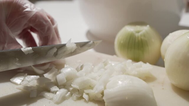 Close-up of chopping onion as the knife gathers small diced pieces on a cutting board. Fresh ingredient prep for soups, sauces, and savory meals.