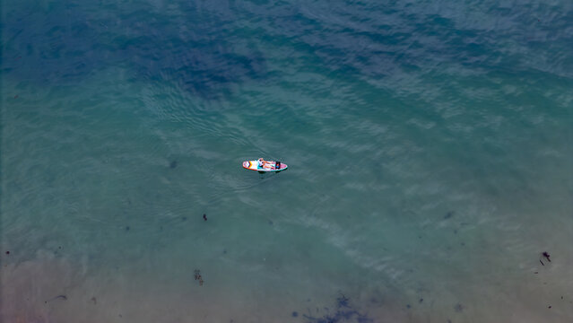 Aerial view of a paddleboarder gliding across the tranquil, turquoise waters, a solitary figure amidst the vast expanse of the ocean, Montecito, California, United States.