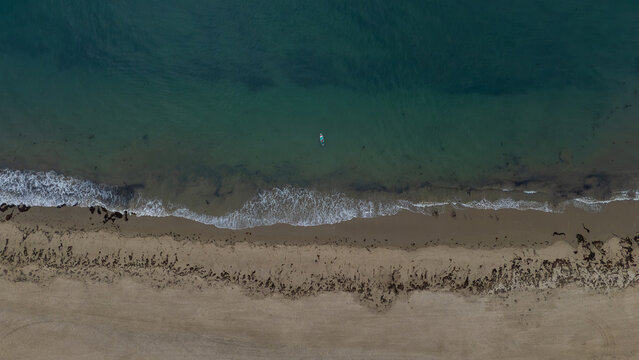 Aerial view of gentle waves kissing the sandy shore, a lone paddleboarder gliding through the turquoise water, Montecito, California, United States.