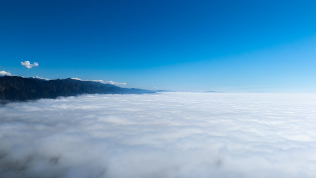 Aerial view of a thick blanket of clouds meeting the dark, rugged mountains under a bright blue sky, Montecito, California, United States.