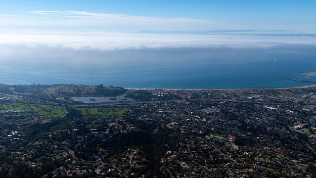 Aerial view of the coastline meeting dense urban development, with fog hugging the horizon, creating a serene yet vibrant scene, Montecito, California, United States.
