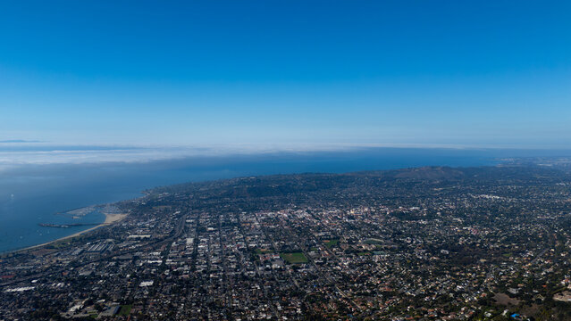 Aerial view of the city nestled between the azure sea and verdant hills, a tapestry of urban life under a boundless sky, Montecito, California, United States.