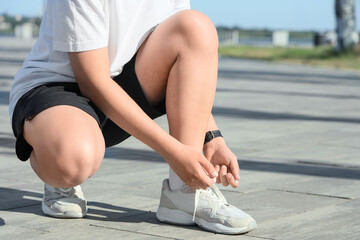 Naklejka premium Male runner tying shoe laces on embankment
