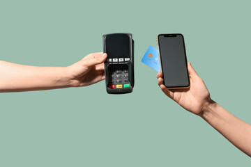 Female hands holding mobile phone with payment terminal and credit card on light turquoise...