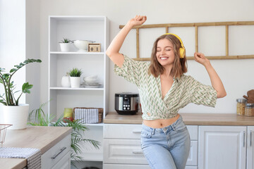 Cool young woman listening to music and dancing in kitchen