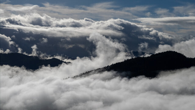 Aerial view of the dark peaks of mountains rise through the thick, swirling clouds like islands in a white sea, Miranda, California, United States.