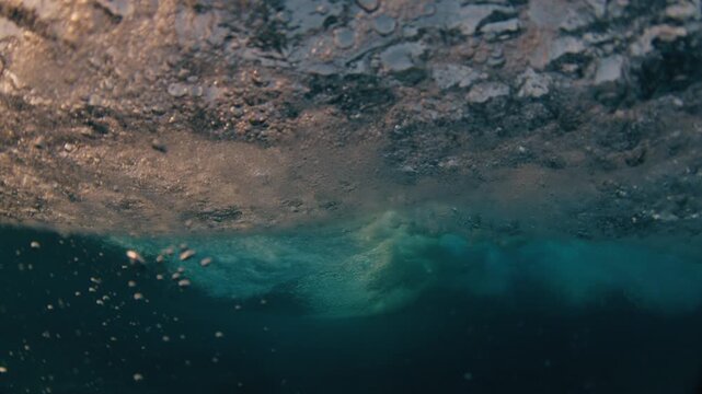Surfer rides the ocean wave in the Maldives and does radical turn with splash into the camera. In water and underwater view of the surfer on the wave