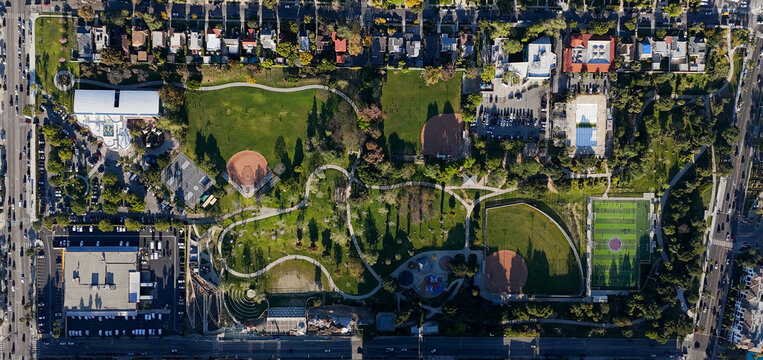 Aerial view of Pan Pacific Park's lush green fields and baseball diamonds contrasting with the surrounding urban grid, Los Angeles, California, United States.