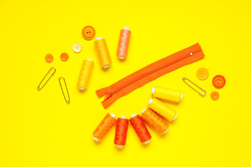 Thread spools with buttons, zipper and pins on yellow background