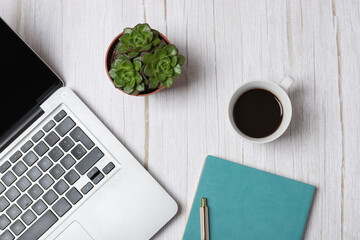 Top view horizontal of laptop, coffee cup, succulents and turquoise notebook on light wooden background, clean and minimal office setup. Concept of modern workspace and lifestyle