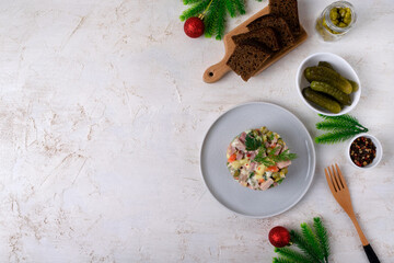 Traditional Russian festive Olivier salad with boiled vegetables and sausages, dressed with mayonnaise on a ceramic plate. Top view on a light background, copy space