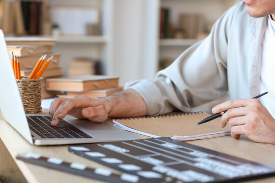 Male screenwriter with laptop writing script at table in office, closeup