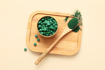 Wooden bowl of spirulina tablets with spoon and powder on beige background