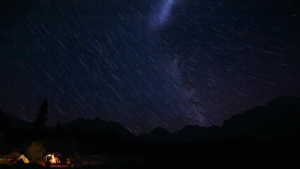 Starting timelapse, camera filming night sky star trails to show Milky Way over camp, with campfire - Powered by Adobe