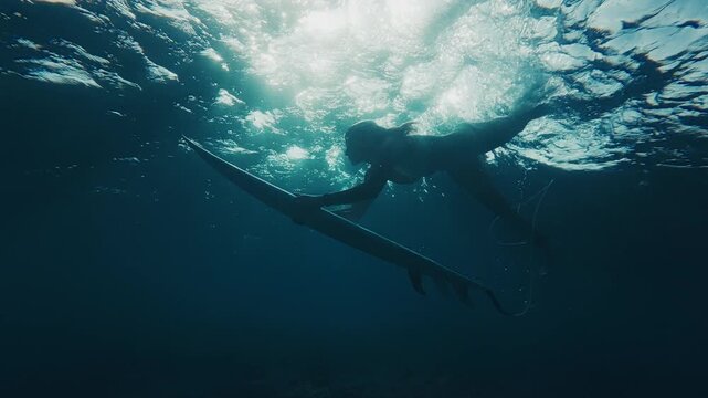 Woman surfer in bikini dives under the ocean wave with surfing board and passes it. Underwater view of the surfer doing duck dive trick