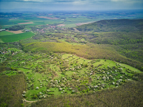 Aerial view of a vibrant tapestry of green forests and open meadows dotted with blooming trees under a vast sky, Pukanec, Nitra Region, Slovakia.