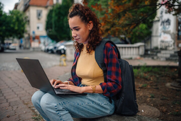 Young student working on laptop outdoors in urban setting