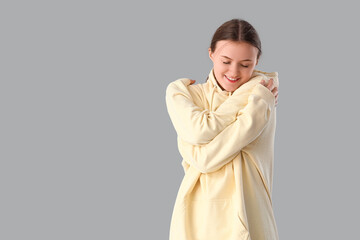 Young woman hugging herself on grey background